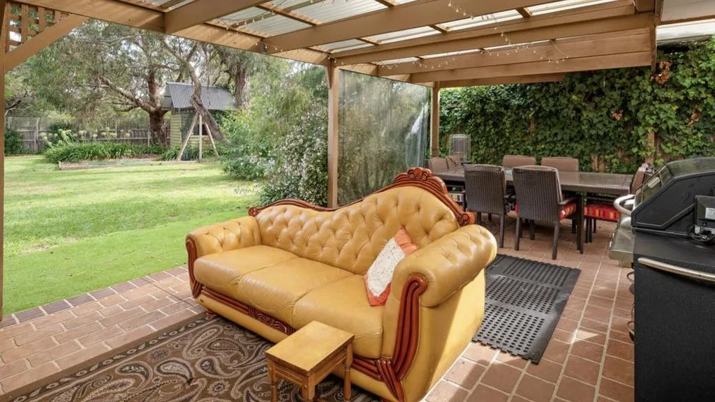 Covered outdoor entertaining area with a leather sofa overlooking a large leafy backyard at Emma and Ben&rsquo;s Mount Martha renovation project.