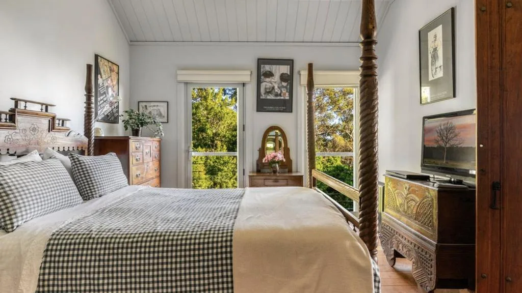 Light-filled bedroom with antique four-poster bed and bushland views at Miriam Margolyes' Southern Highlands home.