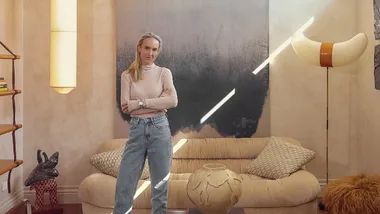 Interior designer Claudia Lambert stands in a beautifully styled living room space with a large blue artwork, beige walls and off white modern sofa
