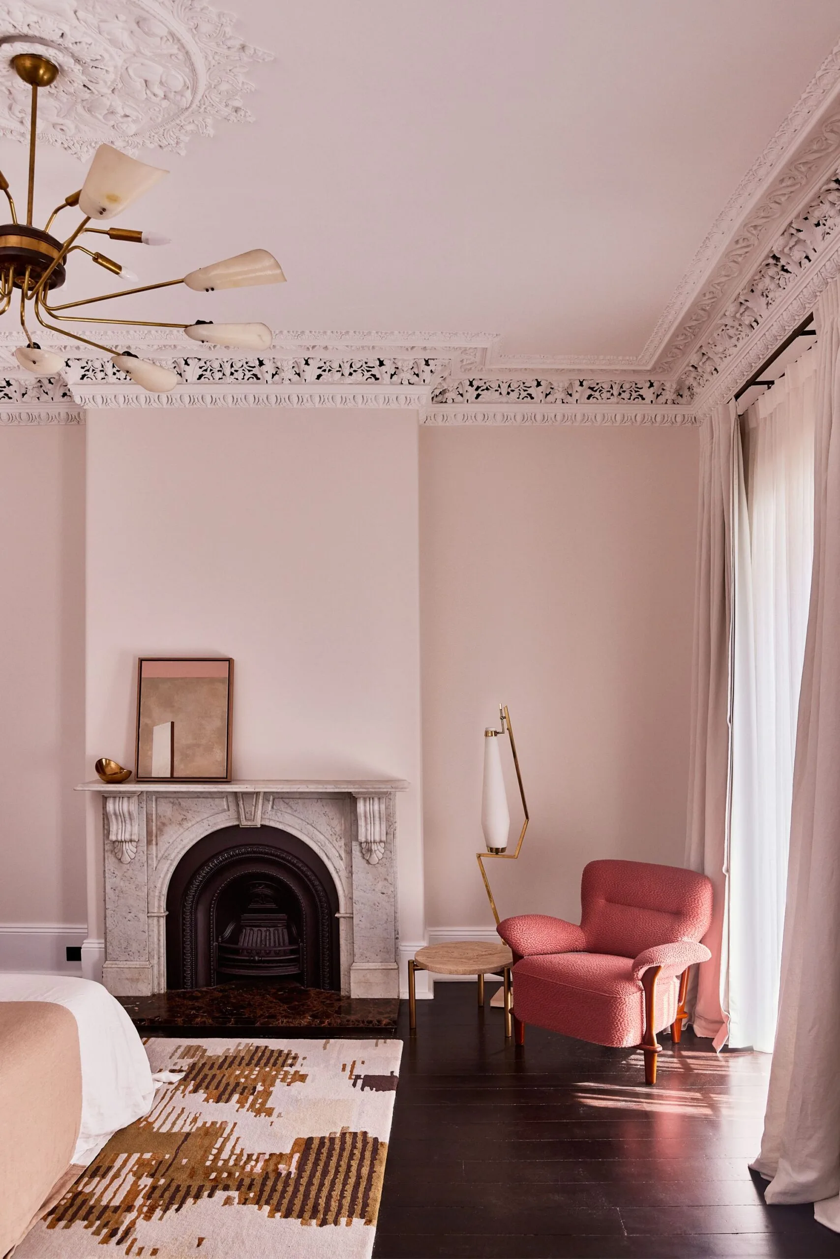 A blush pink bedroom with high ceilings, a built in fireplace and heritage mouldings on the ceiling.