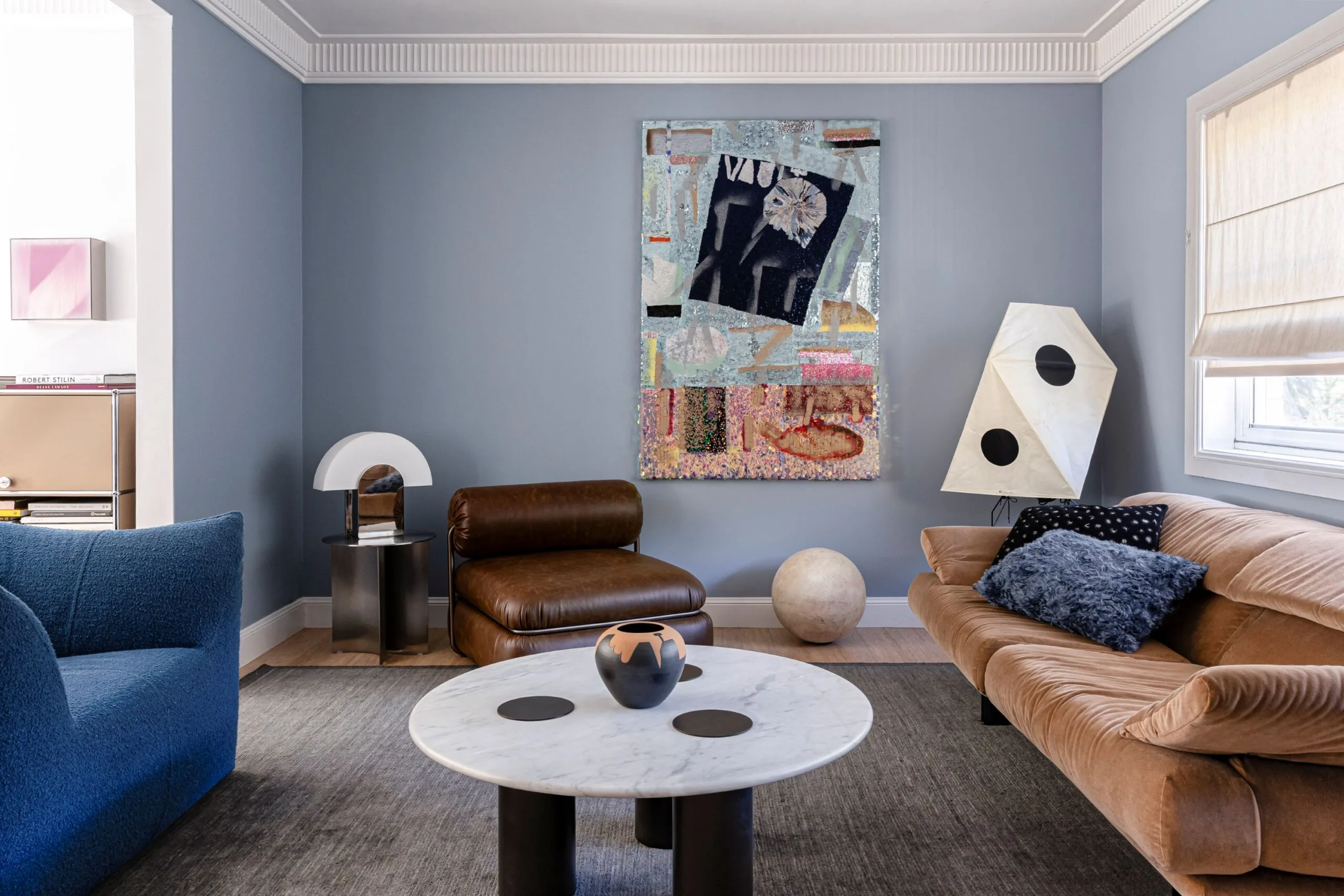 A light blue living room with an abstract painting, a low brown leather arm chair and marble-topped round coffee table