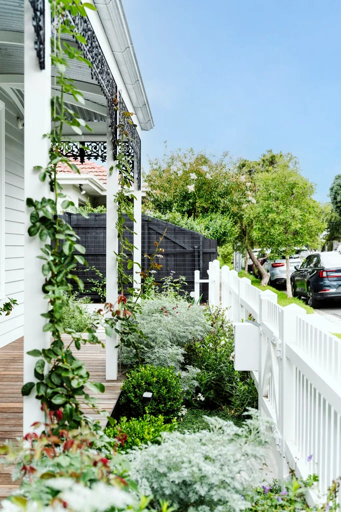 White porch with climbing plants, wooden deck, white picket fence, and green garden on a sunny day.