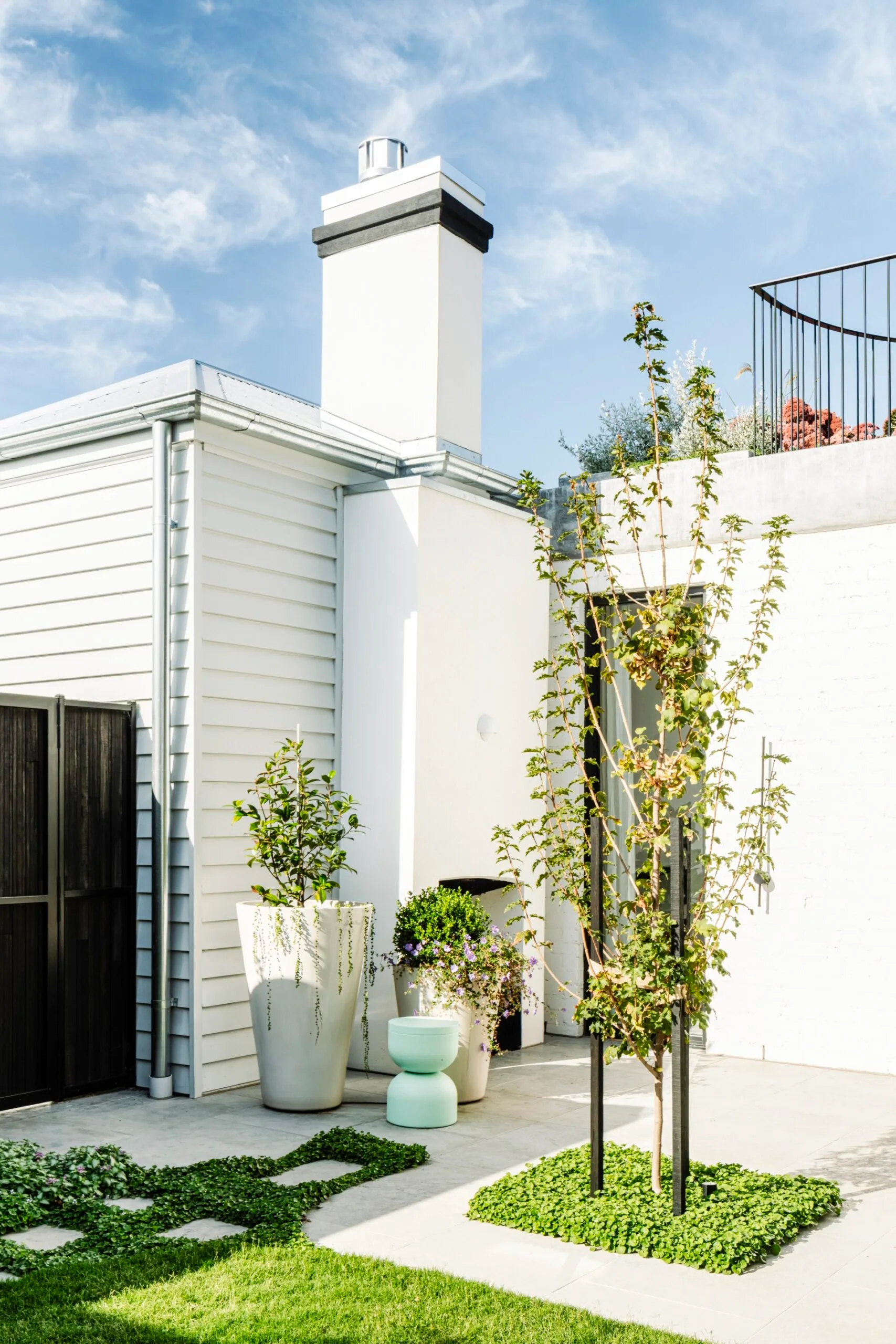 Outdoor patio with potted plants, a chimney, and a small tree against a blue sky.