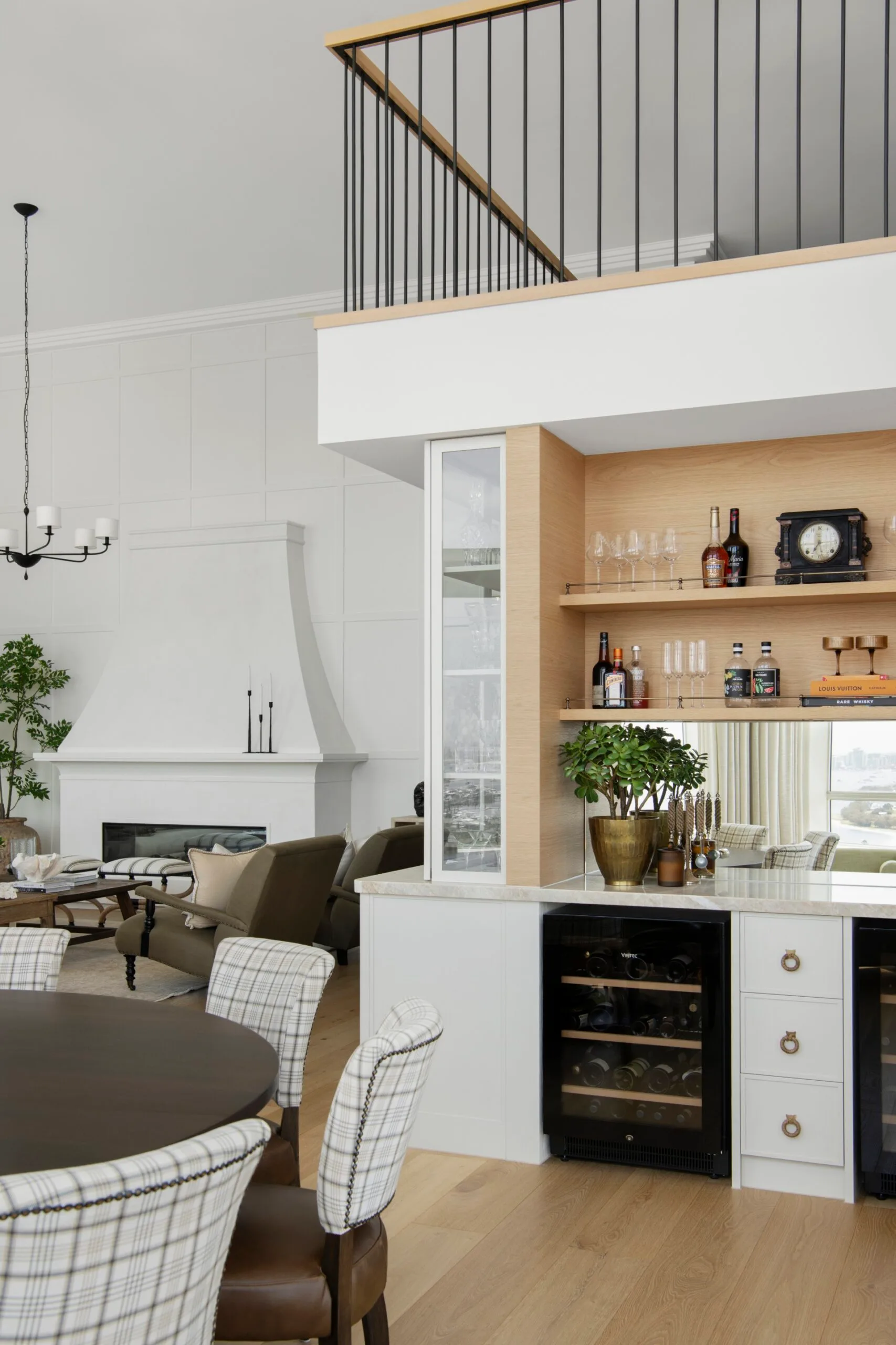 Modern living room with fireplace, bar area, and dining table, featuring neutral tones and wooden accents.