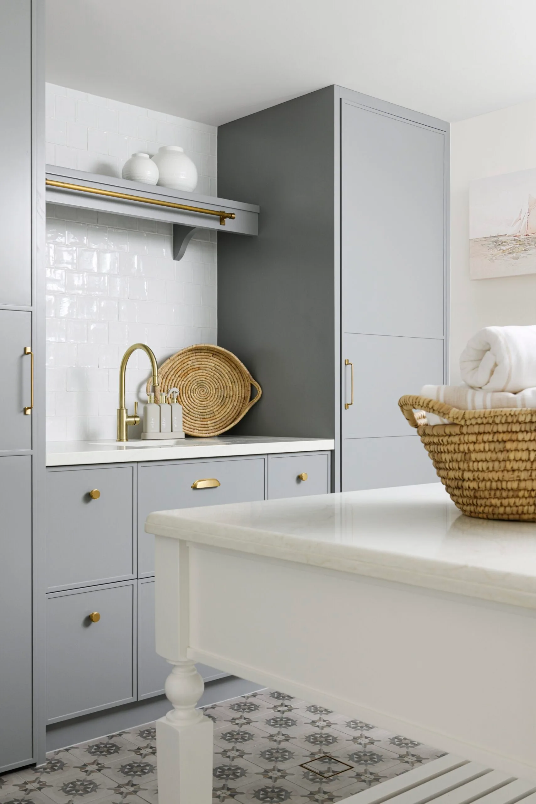 Laundry room with gray cabinets, white countertop, woven basket, and gold faucet.