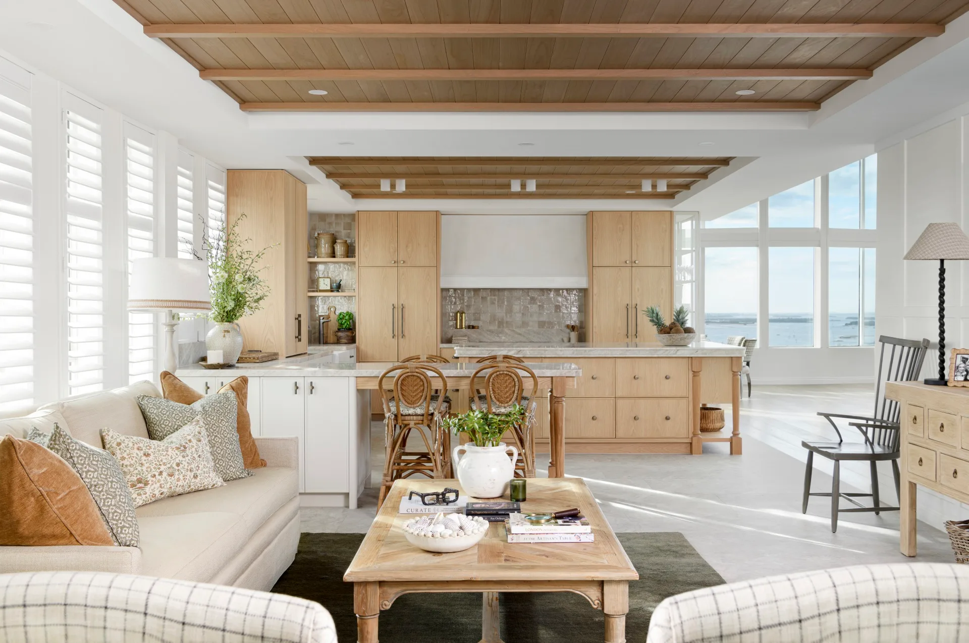 Open-plan kitchen and living room with wooden elements, neutral tones, and sea view through large windows.