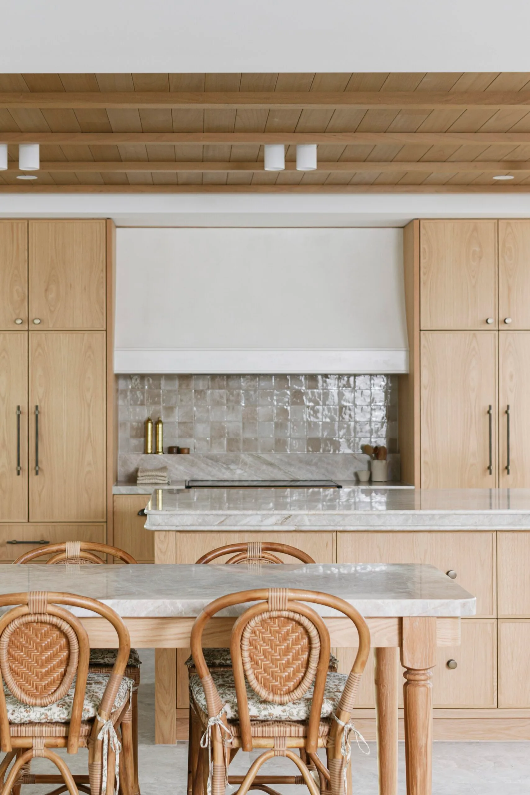 Modern kitchen with wooden cabinetry, woven chairs, marble countertops, and tile backsplash.