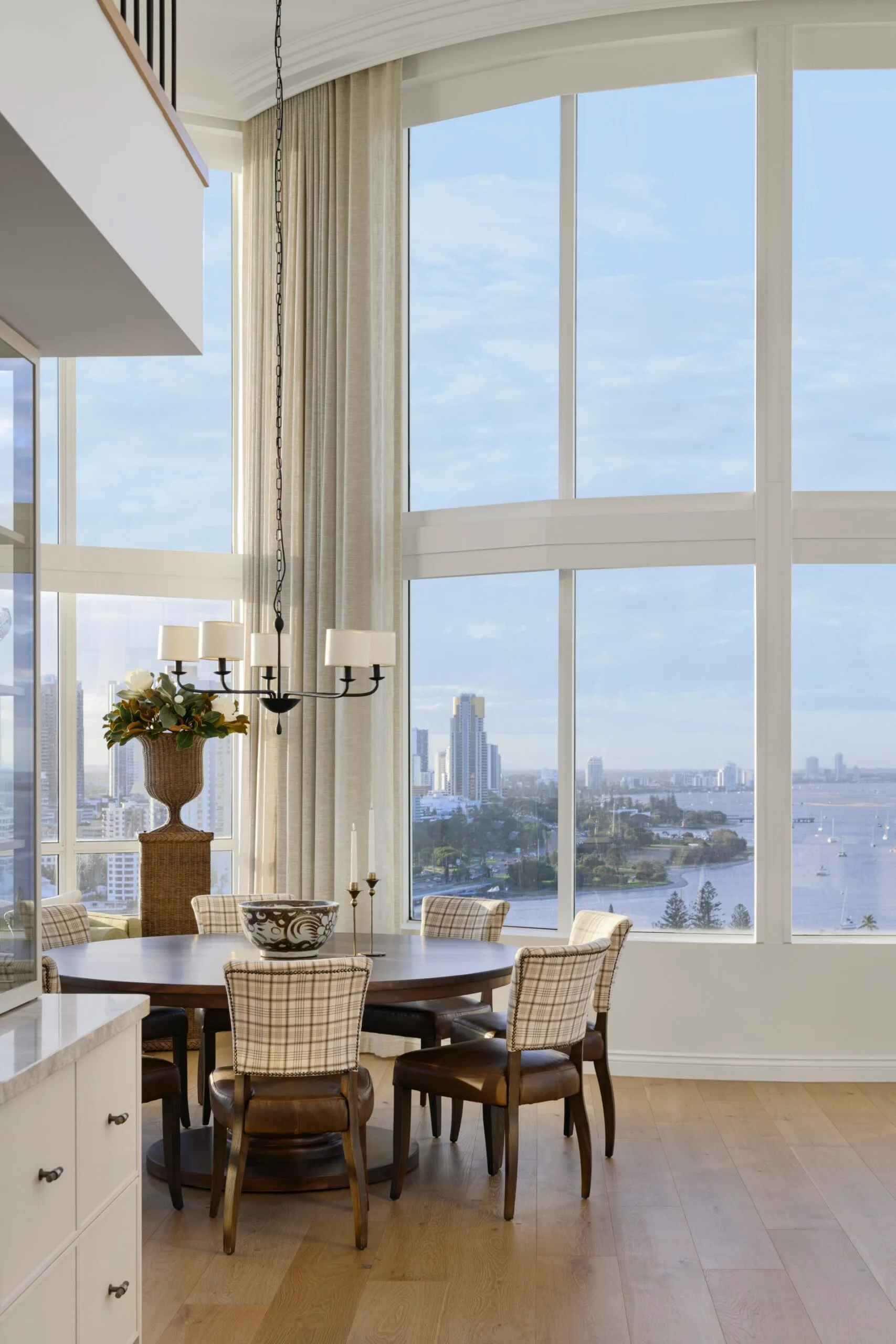 Dining area with round table, plaid chairs, and large windows offering a city and waterfront view.