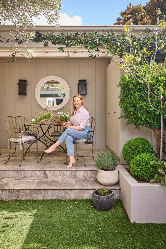 Home Beautiful editor in chief Elle Lovelock seated at her wrought iron outdoor dining setting at home in her greenhouse