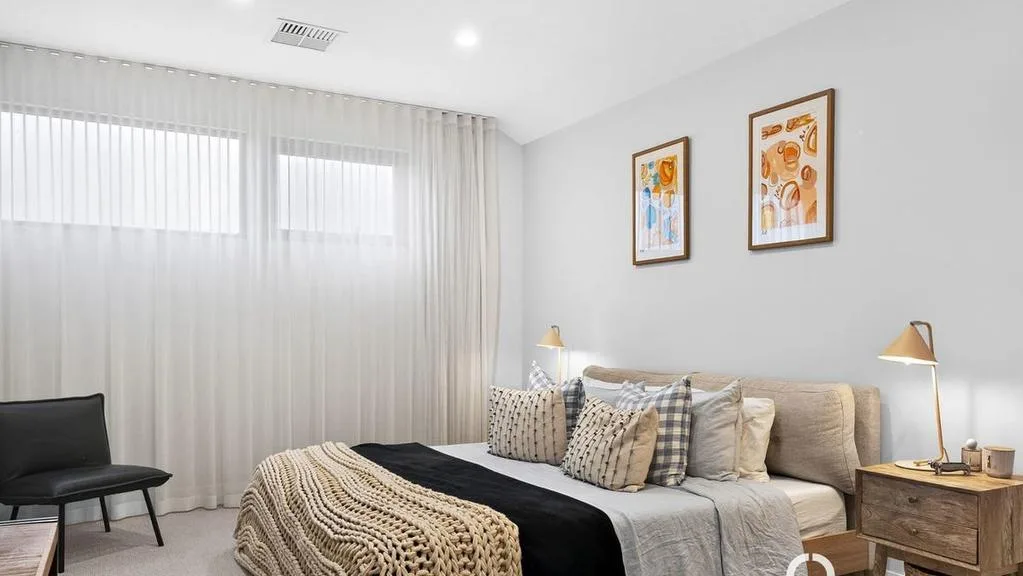 Cozy modern bedroom with neutral tones, layered bedding, two bedside tables with lamps, and framed artwork on the wall.