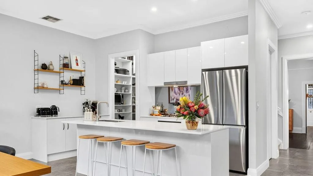 Modern kitchen with white cabinets, stainless steel fridge, island counter with flowers, and bar stools.