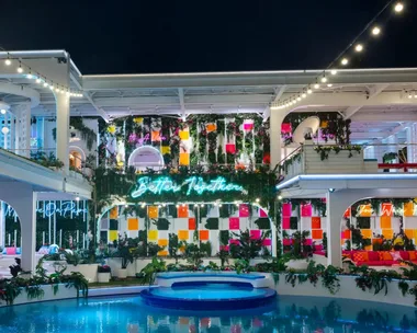 A beautifully lit villa at night with colorful decor, neon signs, and a pool in a tropical setting. This is the Love Island USA villa for 2026.