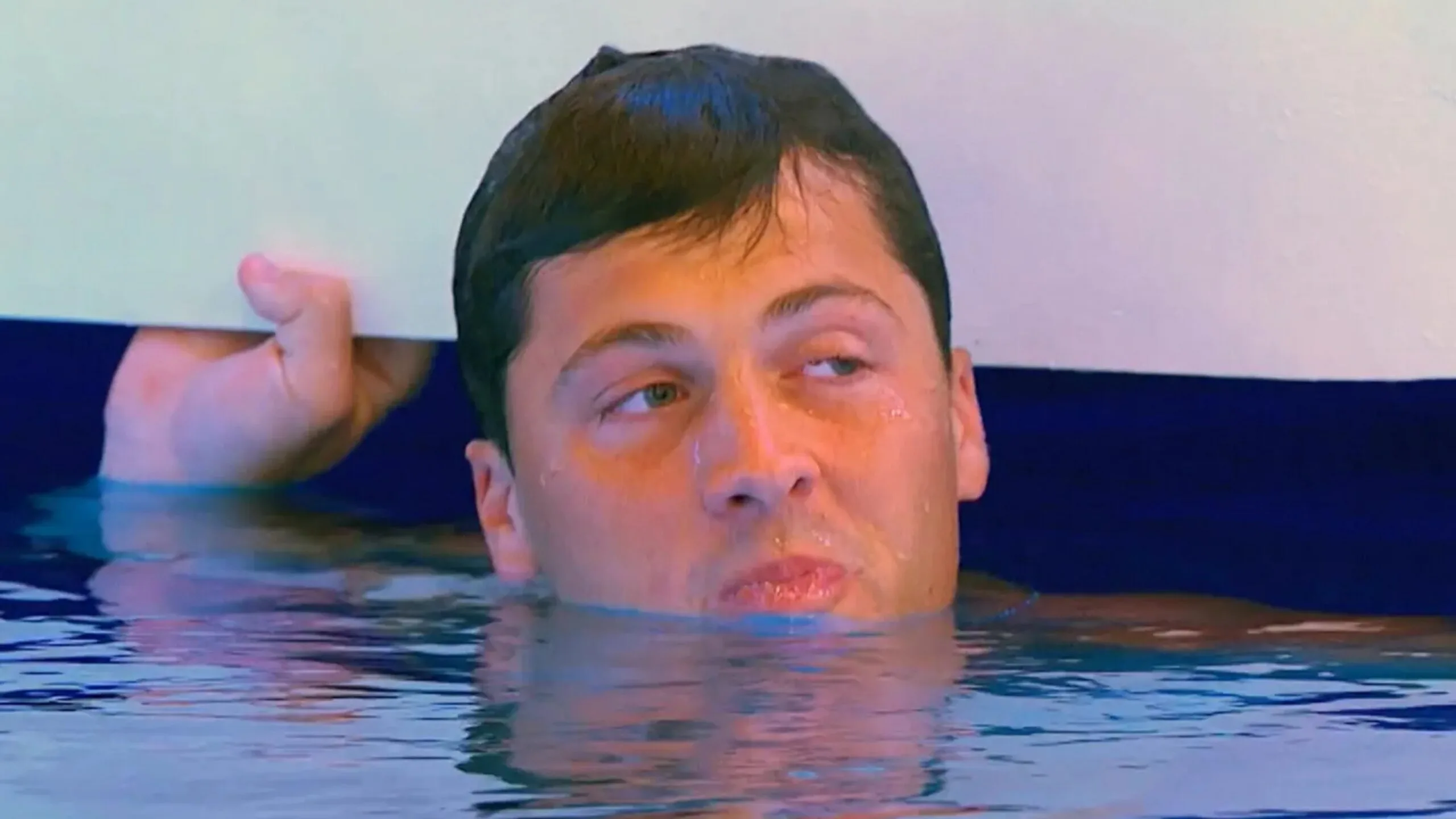 A man partially submerged in water with his hand holding onto a surface, looking sideways. This is a screengrab from Love Island USA season 6 and depicts contestant Rob Rausch.