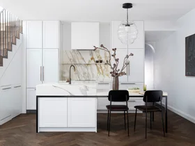 A modern kitchen with white cabinets, a marble island, dark wood flooring, pendant light, and two chairs.