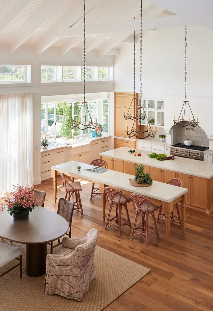 Spacious kitchen with wooden floors, large windows, an island, matching tall table with bar stools that functions as a second island, pendant lights, and a round dining table