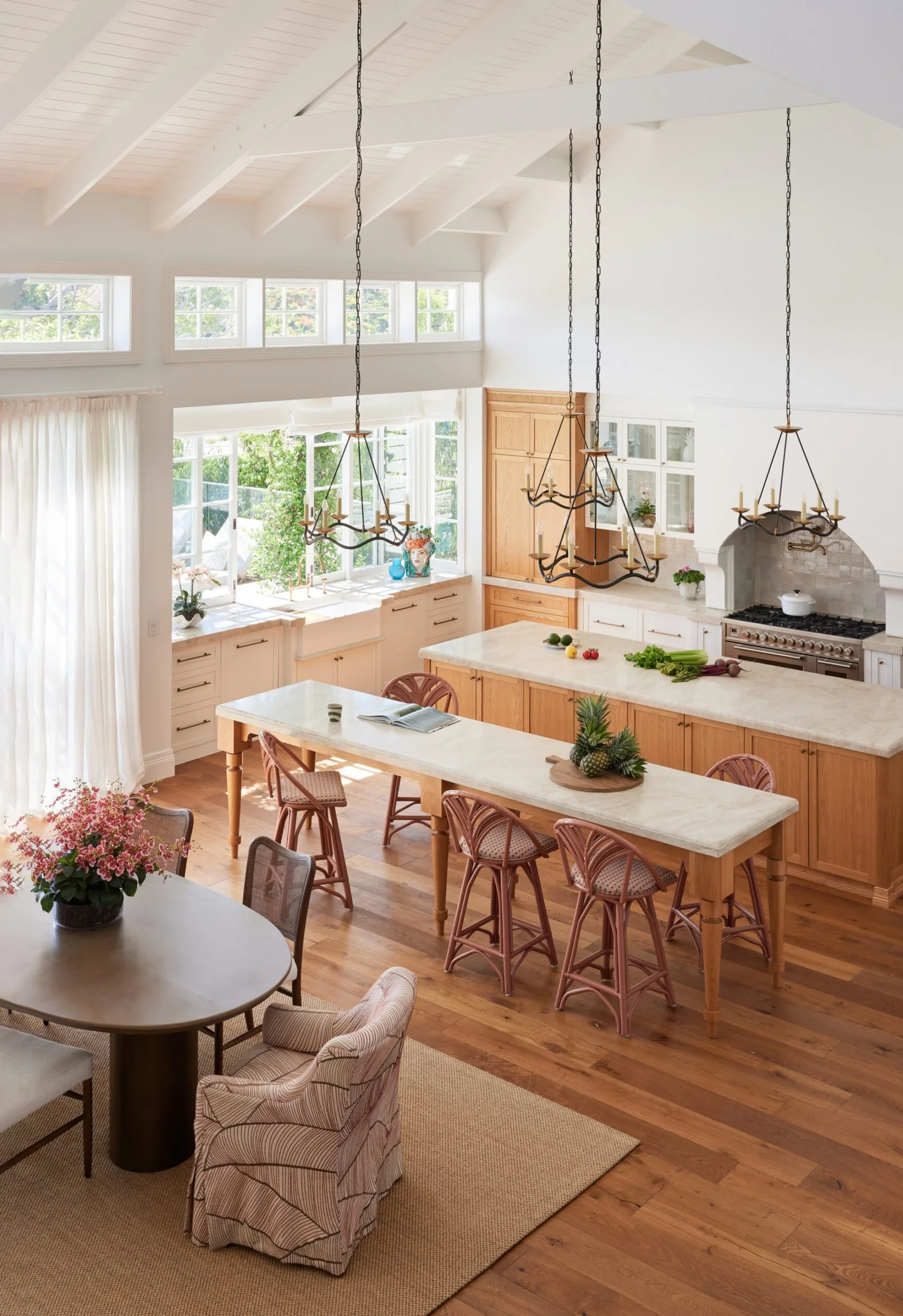 Spacious kitchen with wooden floors, large windows, an island, matching tall table with bar stools that functions as a second island, pendant lights, and a round dining table