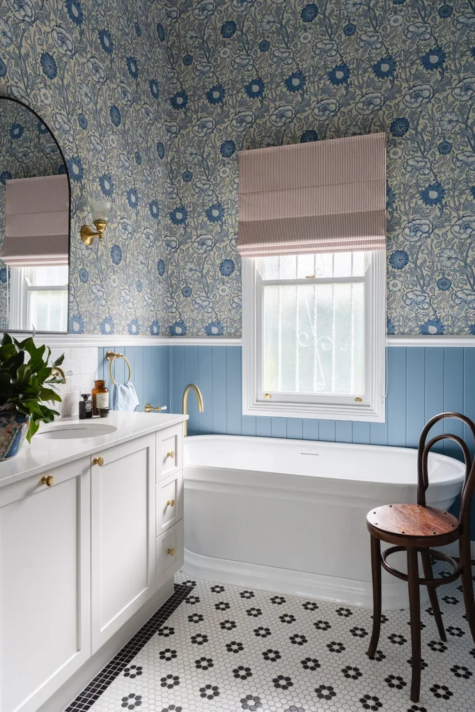 Elegant bathroom with blue floral wallpaper, striped blinds, white bathtub, and patterned floor tiles.