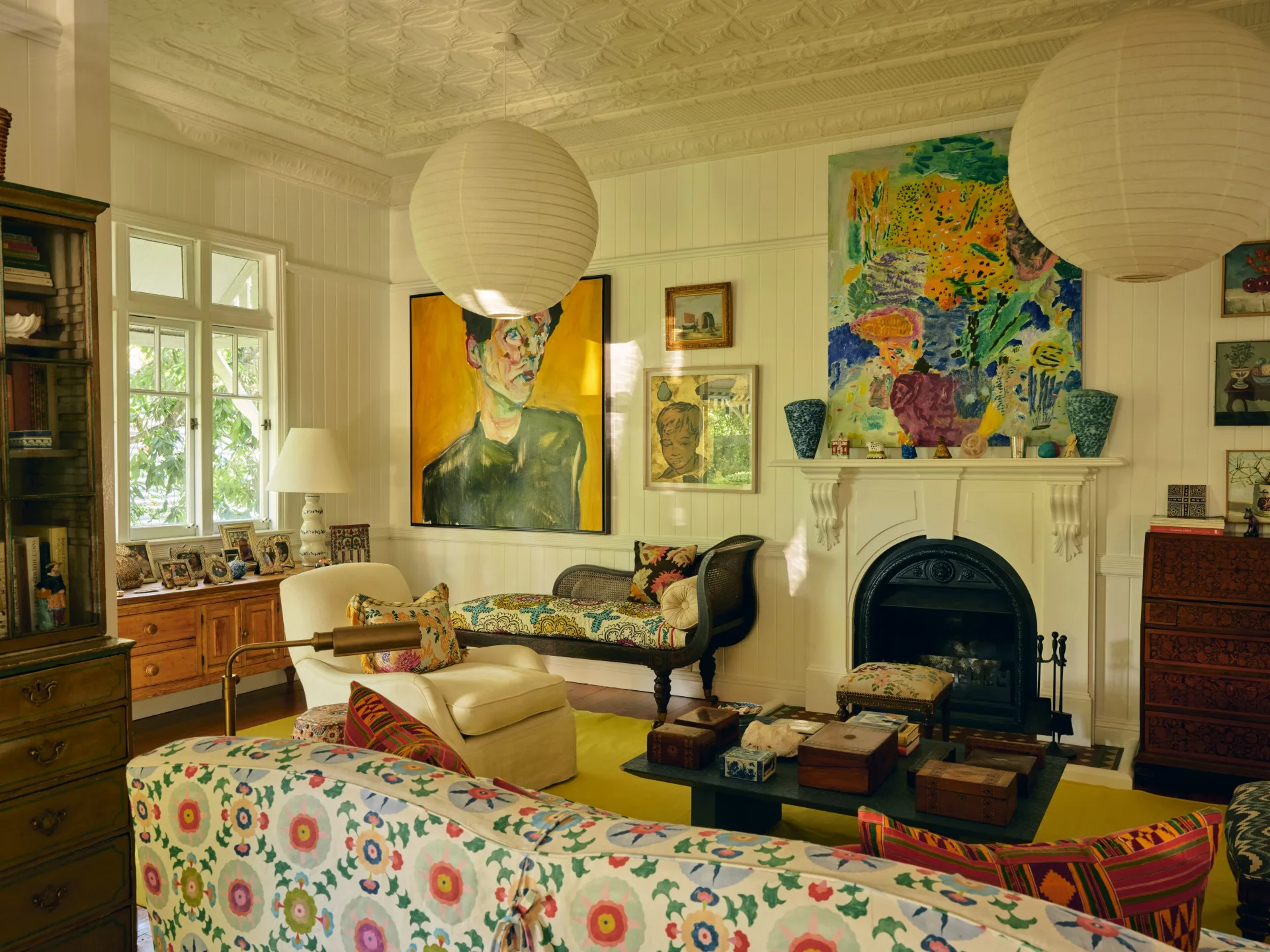 Cozy living room with colorful artwork, floral sofa, white walls, a fireplace, and large paper lanterns hanging from the ceiling.