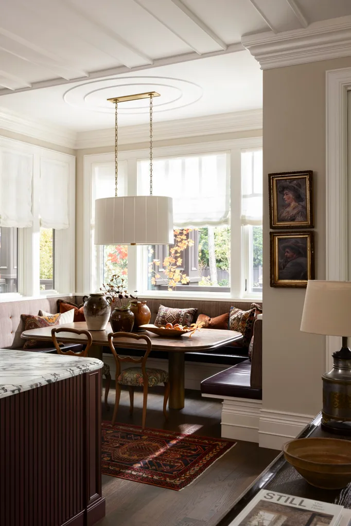 Cozy dining nook with a wooden table, chairs, and bench seating, decorated with vases, pillows, and wall art.