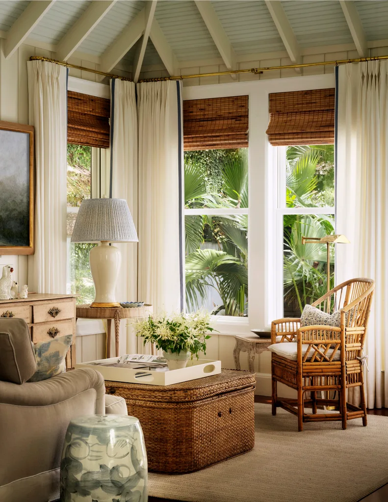 Cozy living room corner with wicker chair, basket coffee table, lamp, and window view of tropical greenery.