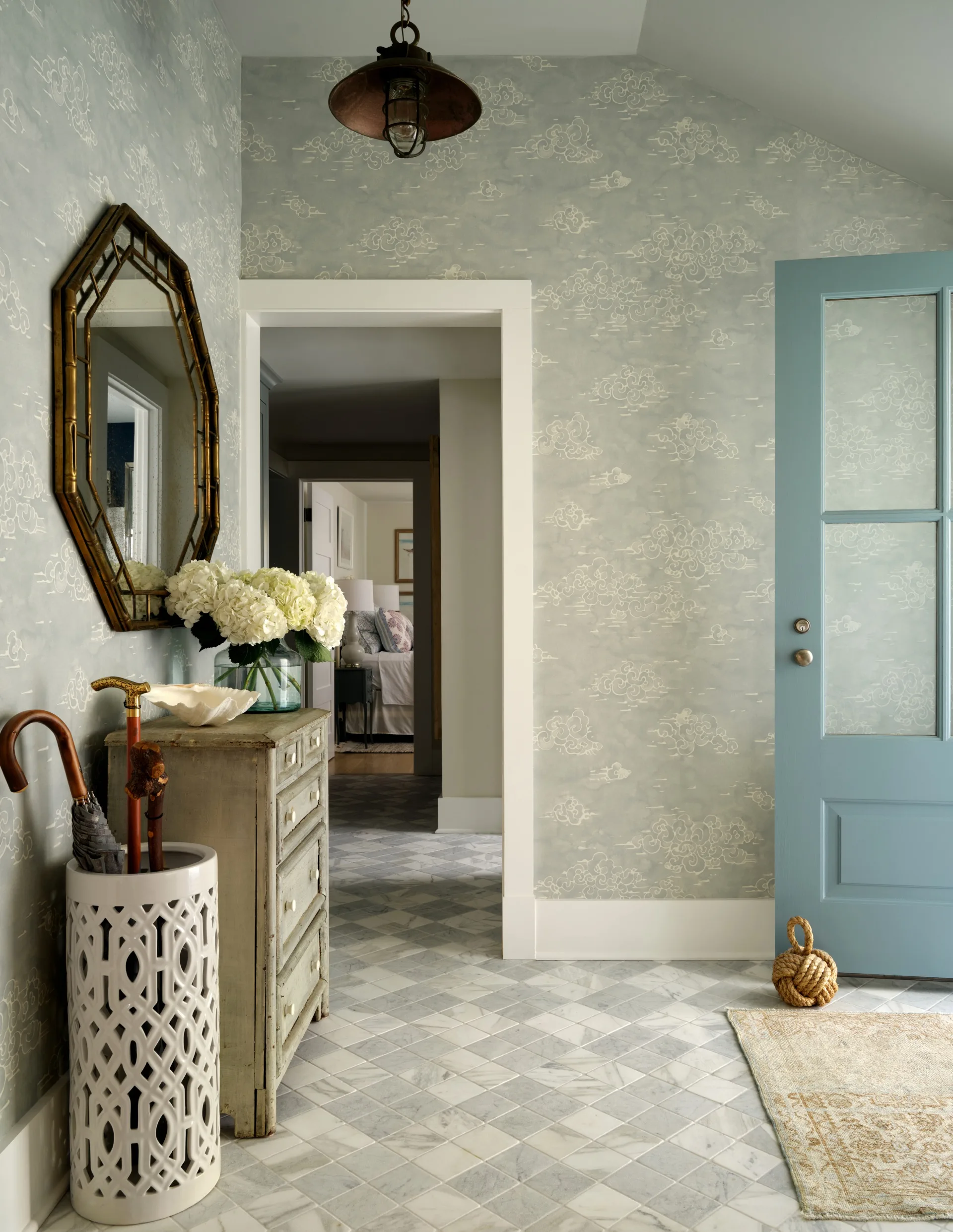 Elegant hallway with patterned wallpaper, a decorative mirror, and blue door. Marble floor with ornate umbrella stand.