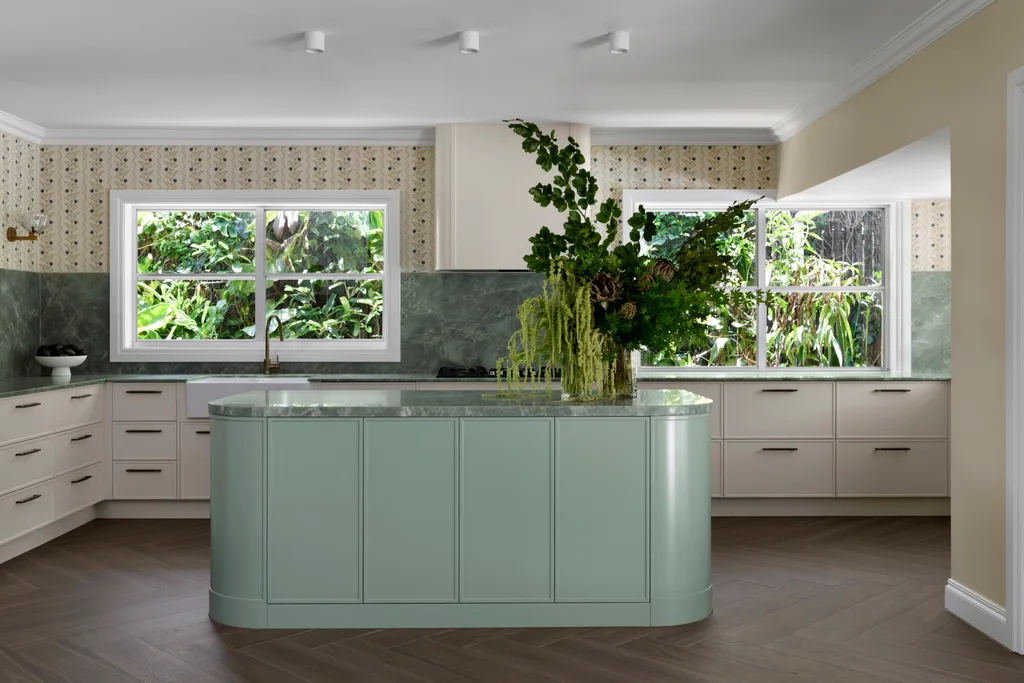 Modern kitchen with green island, white cabinets, large windows, and lush outdoor view.