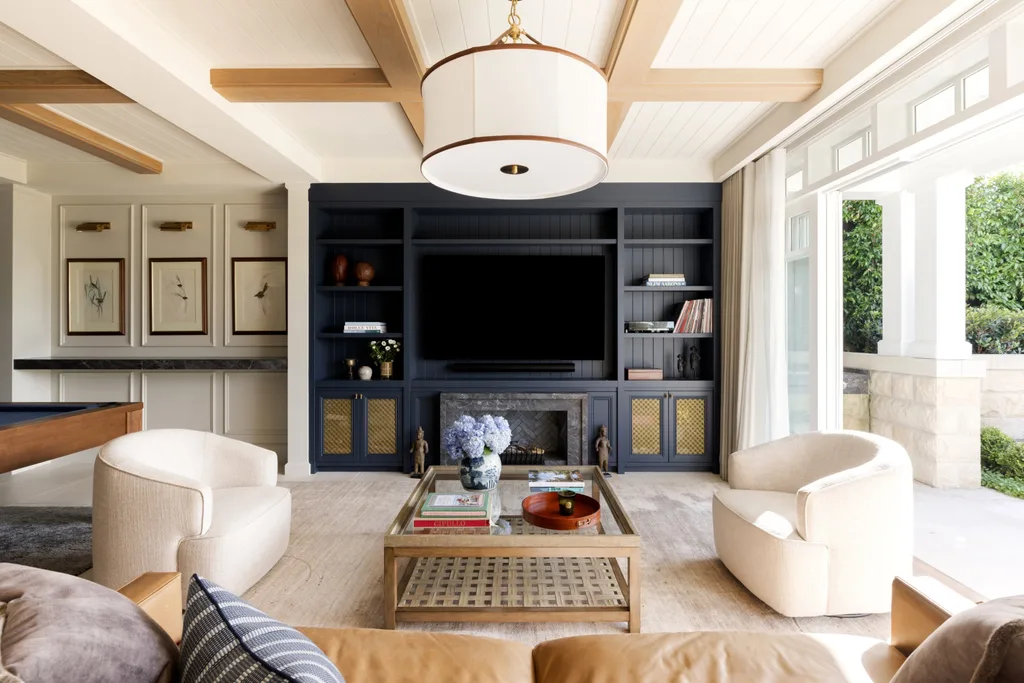 Luxurious living room with modern furniture, a large TV, and built-in navy shelves, featuring ceiling beams and natural light.