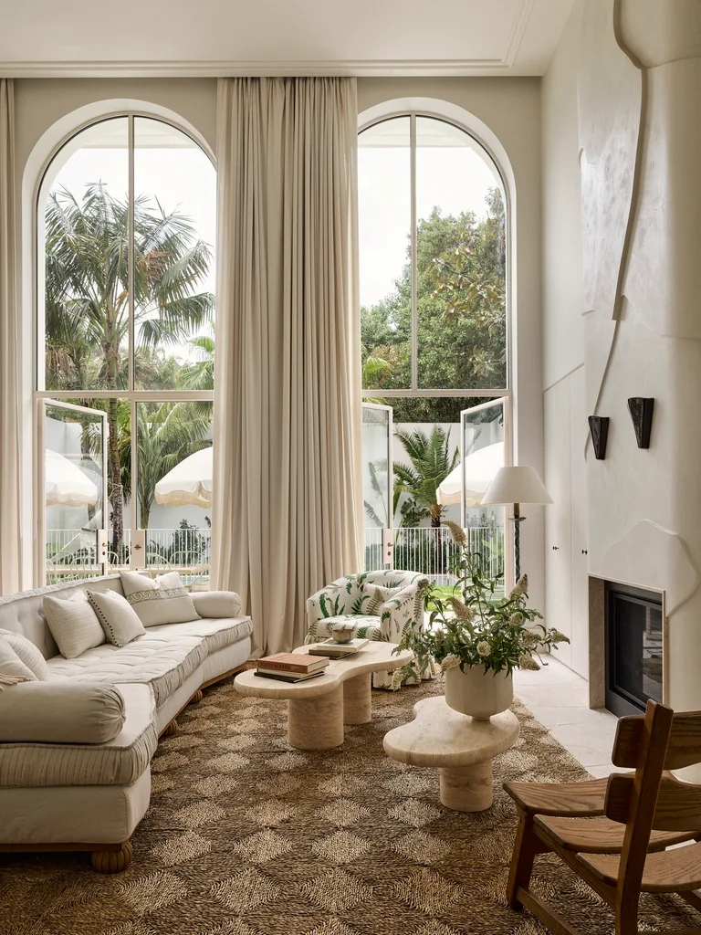 Elegant living room with large arched windows, white sofa, patterned carpet, and green plants.