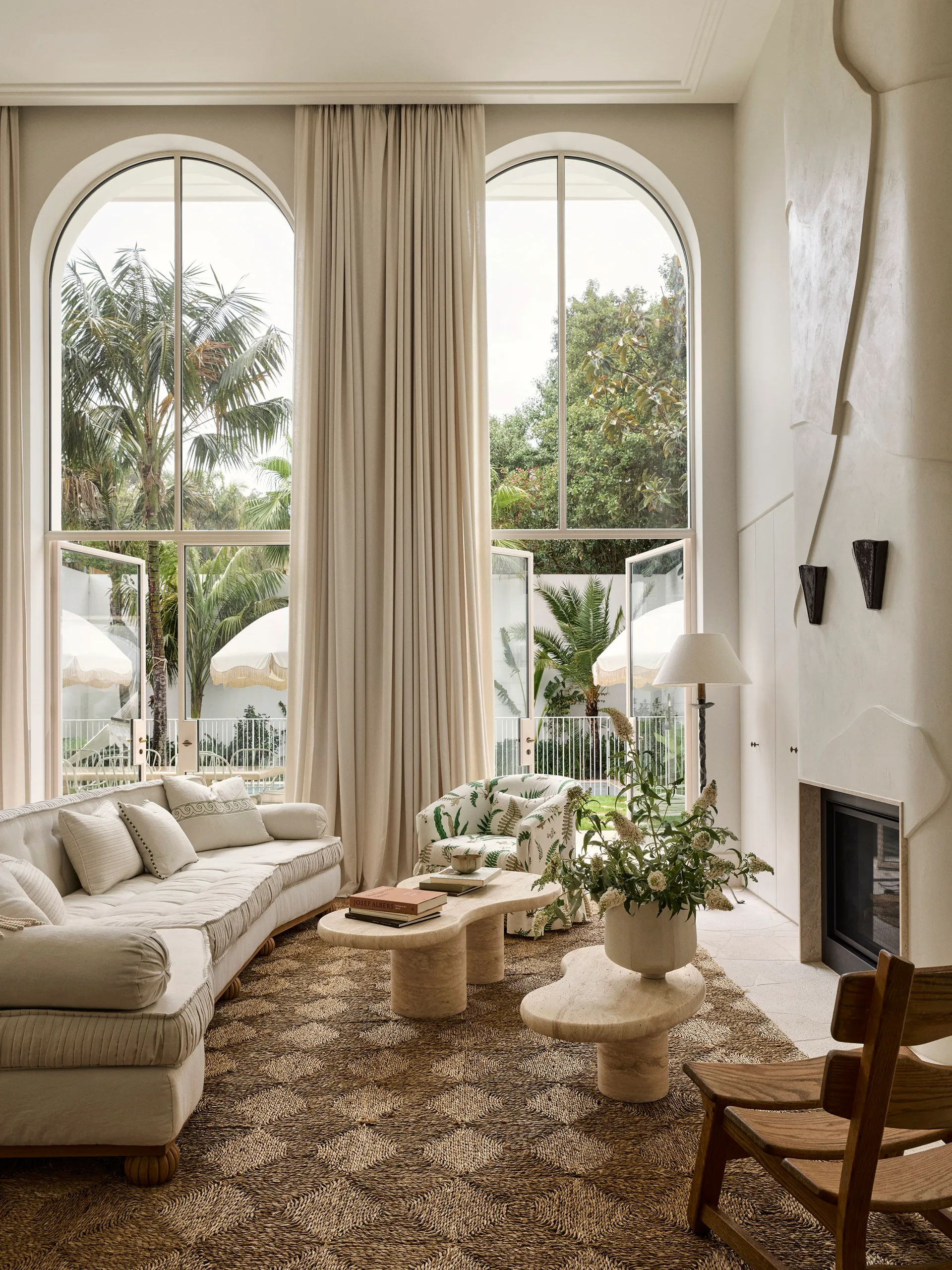Elegant living room with large arched windows, white sofa, patterned carpet, and green plants.