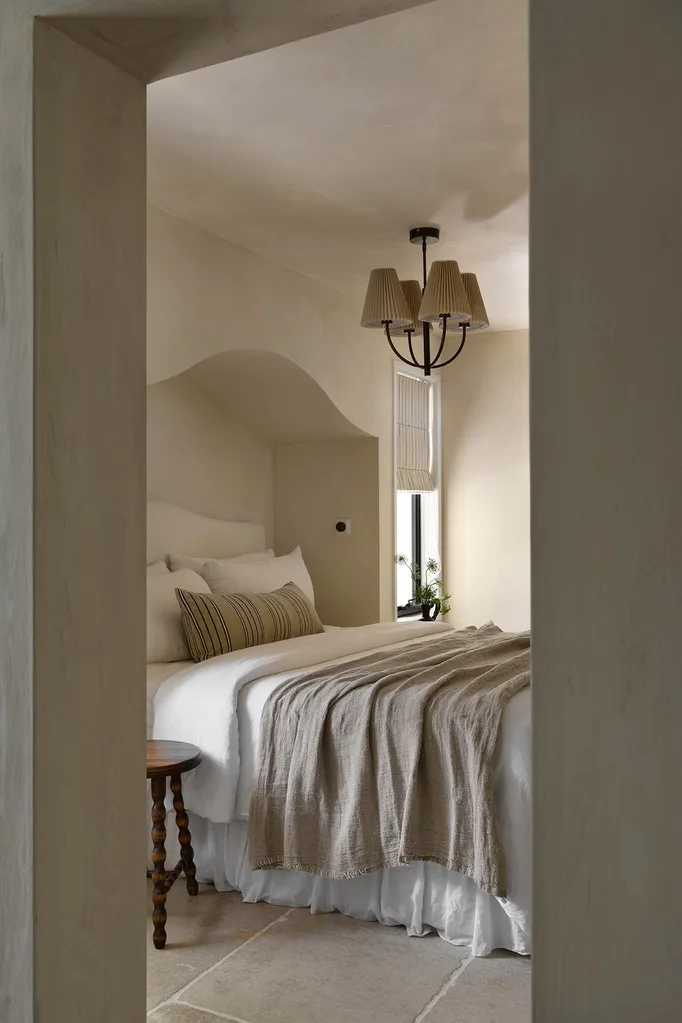 Cozy bedroom with a large bed, earthy tones, a soft throw, wooden accents, and a window with natural light.