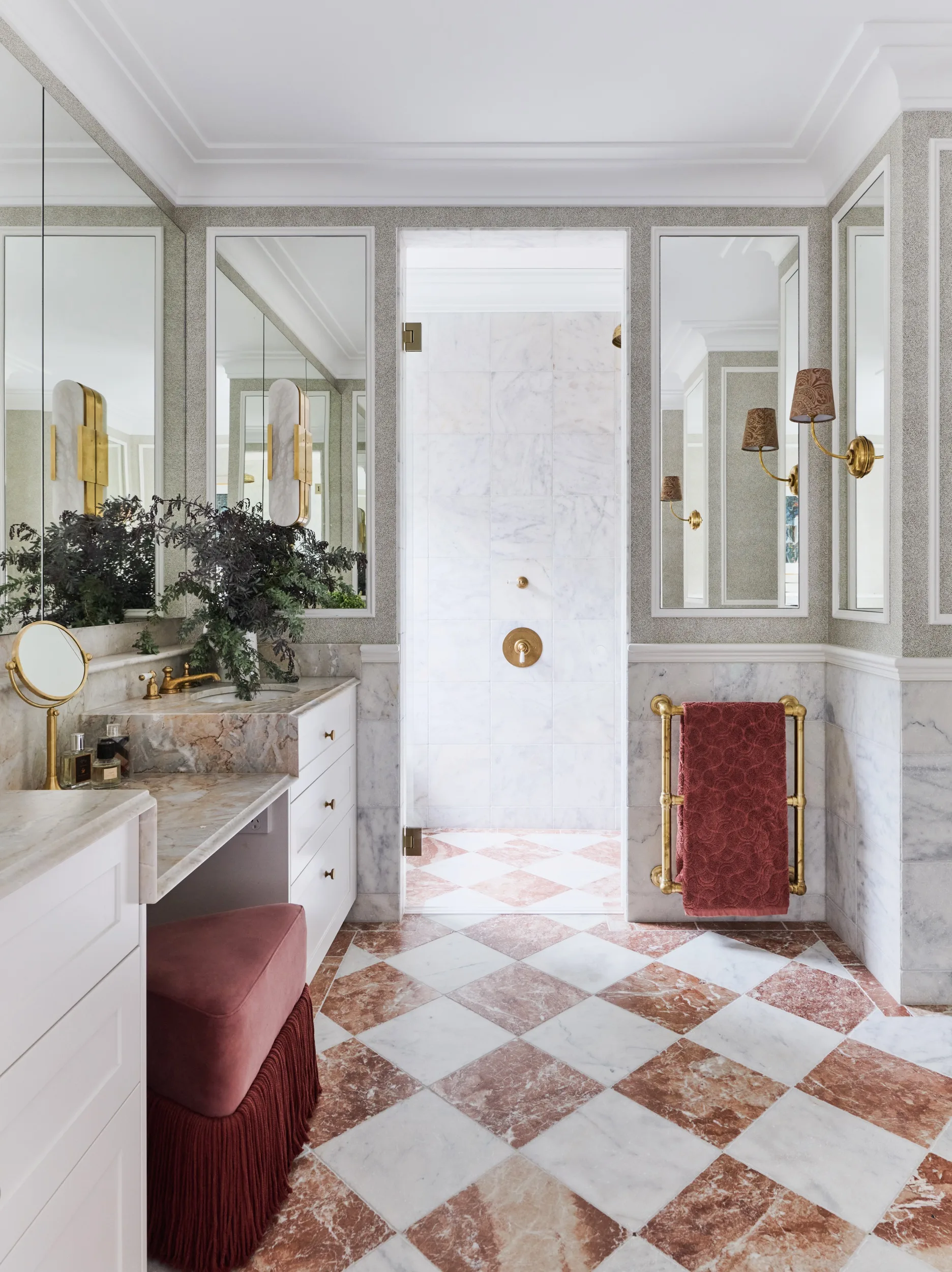 Luxurious marble bathroom with gold fixtures, large mirrors, plants, and checkered floor.