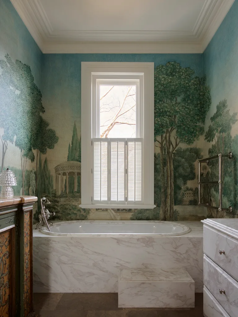 Marble bathtub in a bathroom with scenic forest wall mural and a window with shutters.