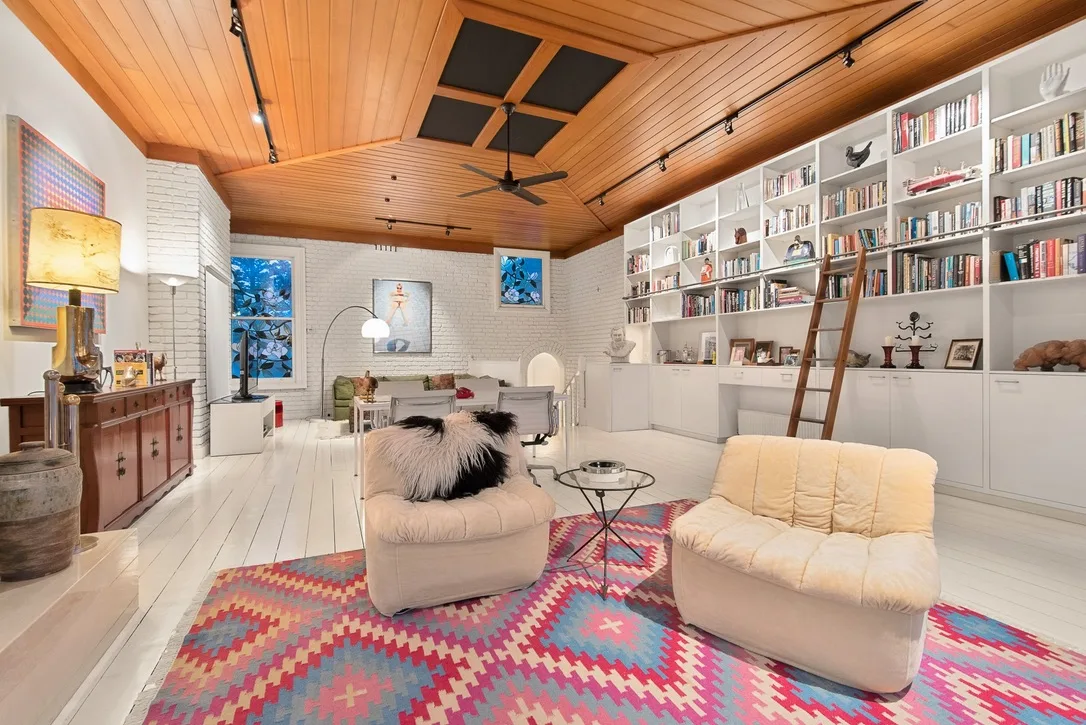 Mid-century modern living room with white shelves, colorful rug, cozy seating, and wooden ceiling Ron Barassi St Kilda home
