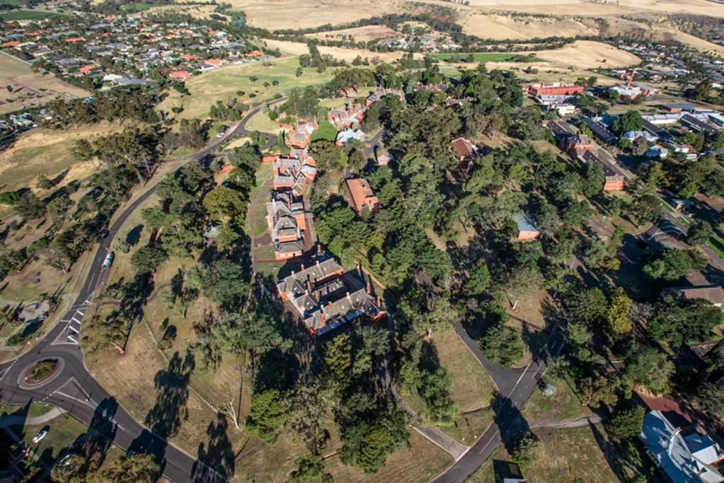 Aerial view of a historical building complex surrounded by trees and roads in a rural setting.