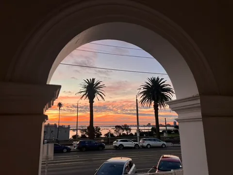 Sunset view through an archway, showing palm trees and calm waters under a colorful sky.