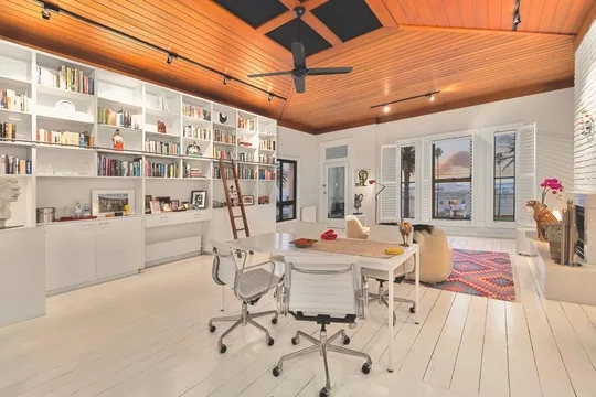 A spacious, modern living room with white furniture, bookshelves, a fireplace, and large windows overlooking a scenic view.
