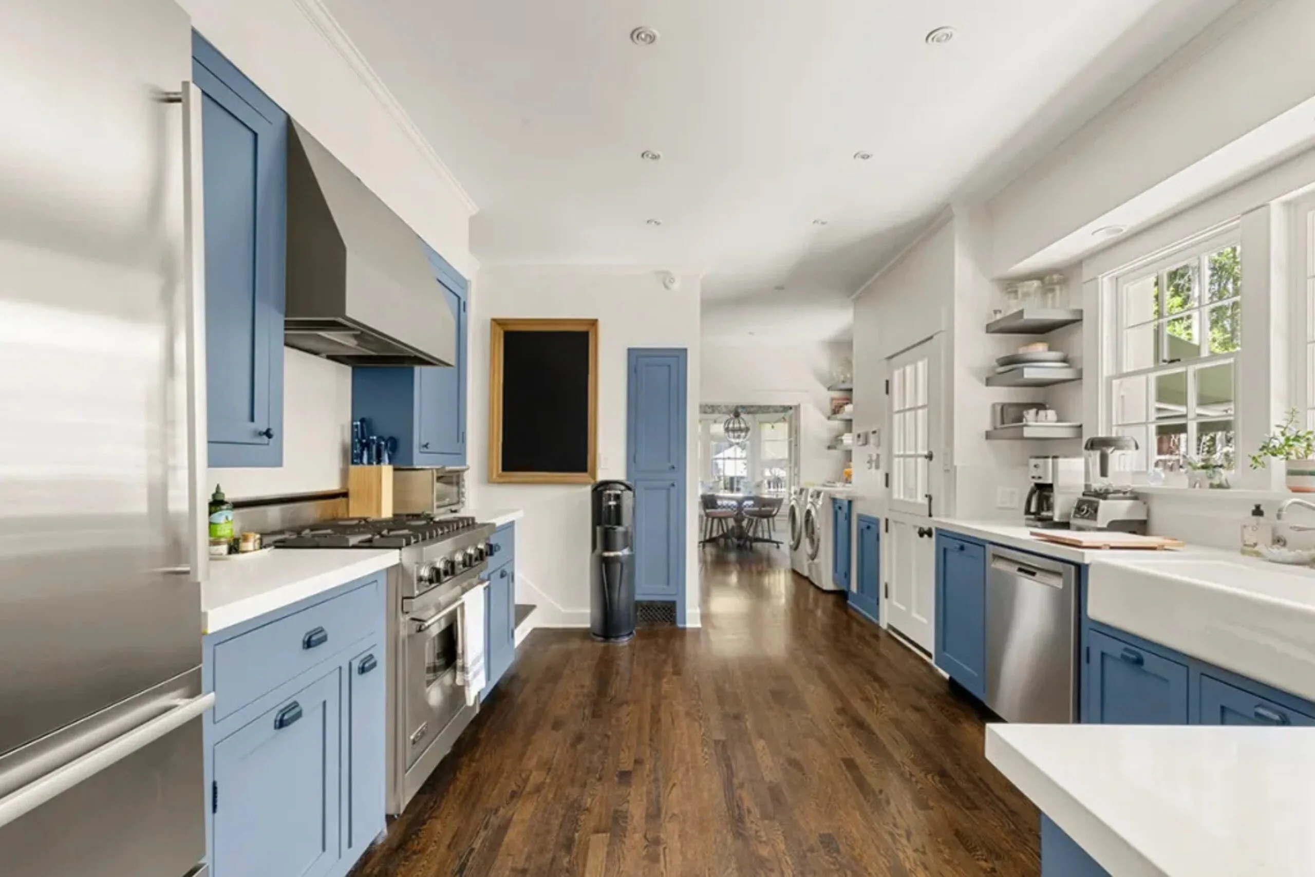 Spacious kitchen with blue cabinets, stainless steel appliances, hardwood floors, and a view of the dining area. Amanda Seyfried's Los Angeles home.