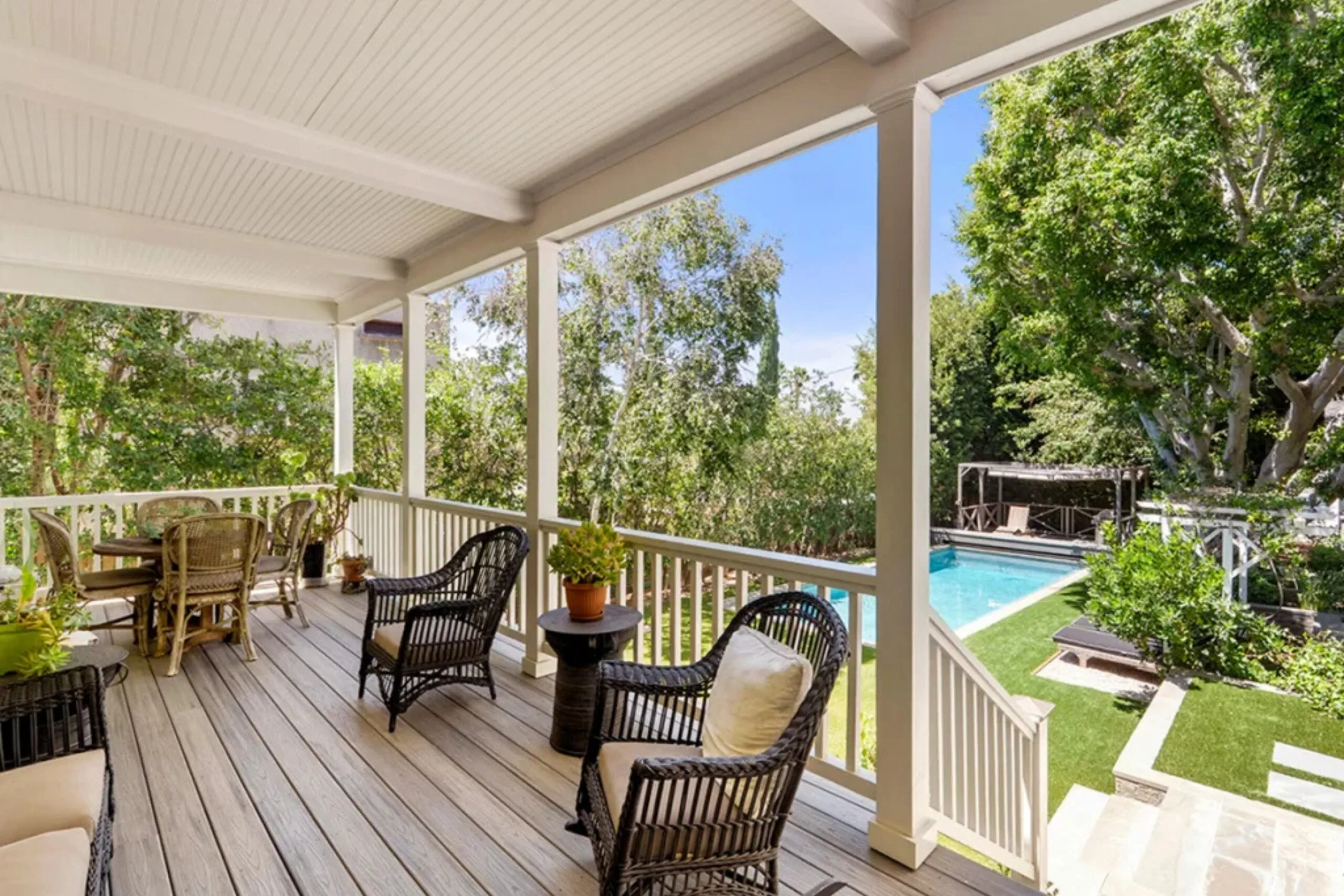 Covered porch with wicker furniture overlooking a garden and swimming pool.