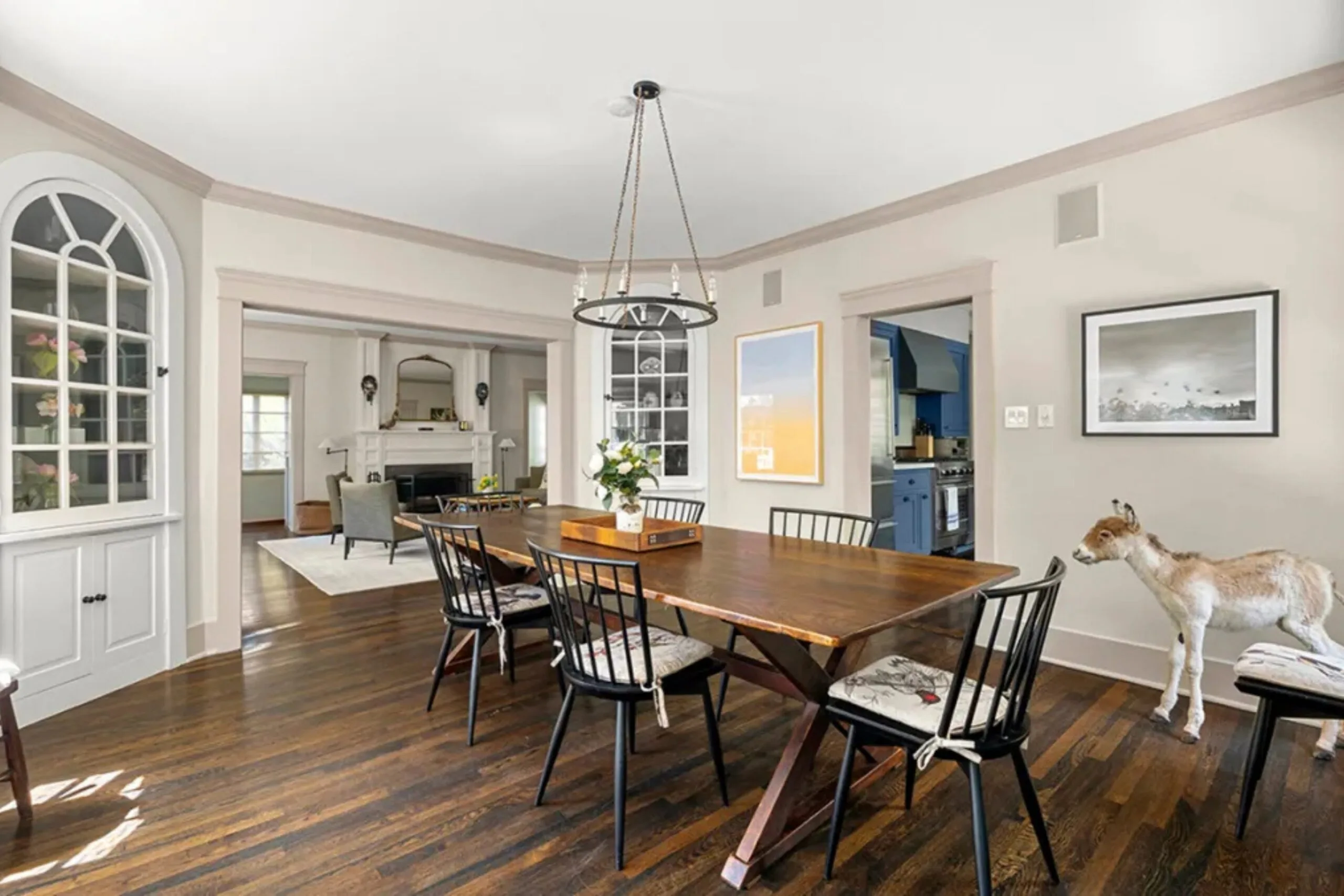 Dining room with a wooden table, black chairs, chandelier, and a small goat standing near the chairs. Amanda Seyfried's Los Angeles home.
