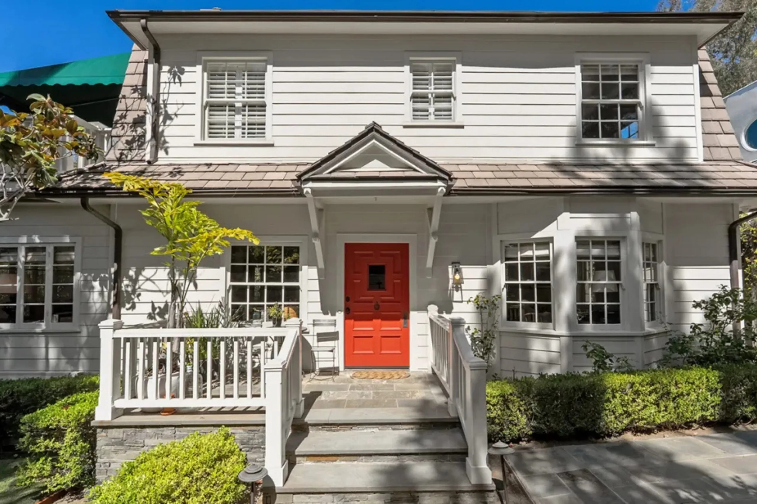 White house with red door, shuttered windows, and foliage, viewed from the front with steps leading to the entrance. Amanda Seyfried's Los Angeles home.