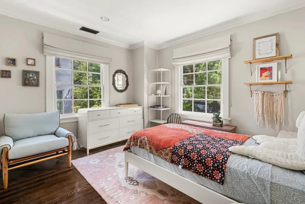 Bright bedroom with a large window, white dresser, and a bed with colorful bedding.