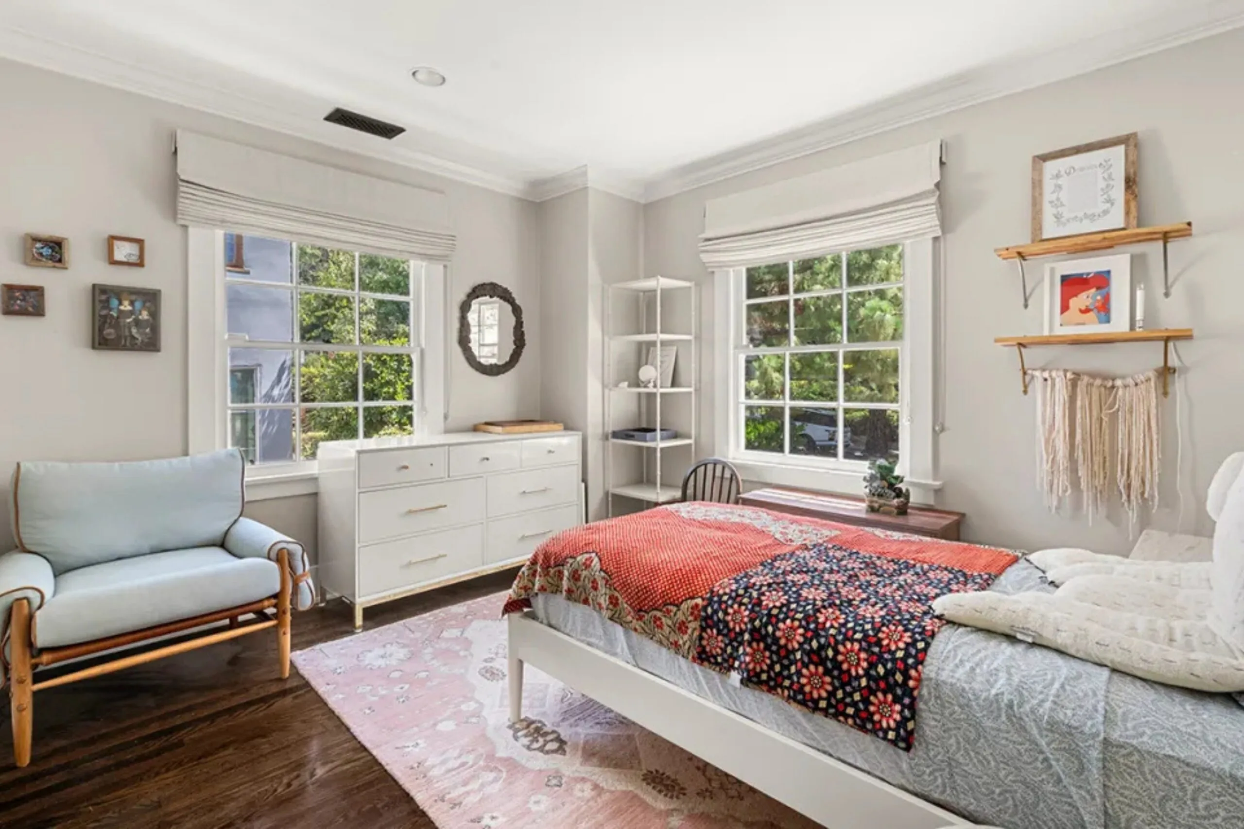 Bright bedroom with a large window, white dresser, and a bed with colorful bedding.