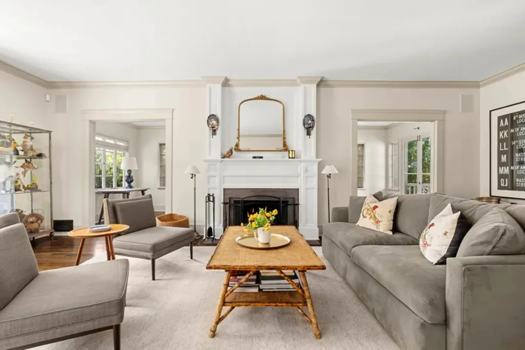 Living room with gray sofa, armchairs, coffee table with flowers, fireplace, and large mirror above mantel. Amanda Seyfried's Los Angeles home.