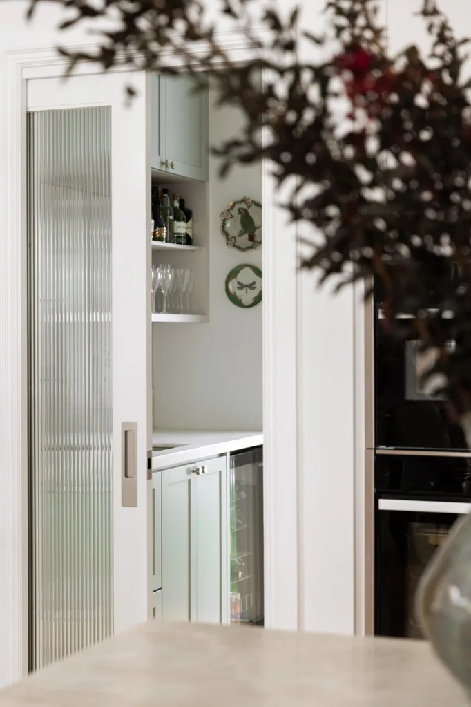 Sliding door reveals bar area with liquor bottles, glasses, and decorative plates.