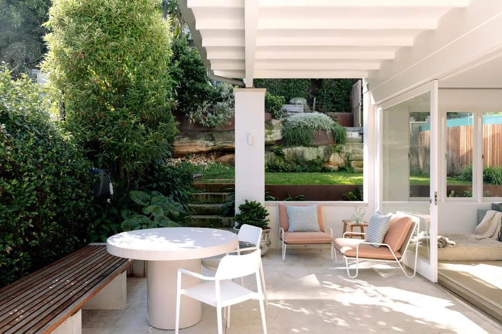 Outdoor patio with white furniture, green plants, a wooden bench, and glass doors leading inside.