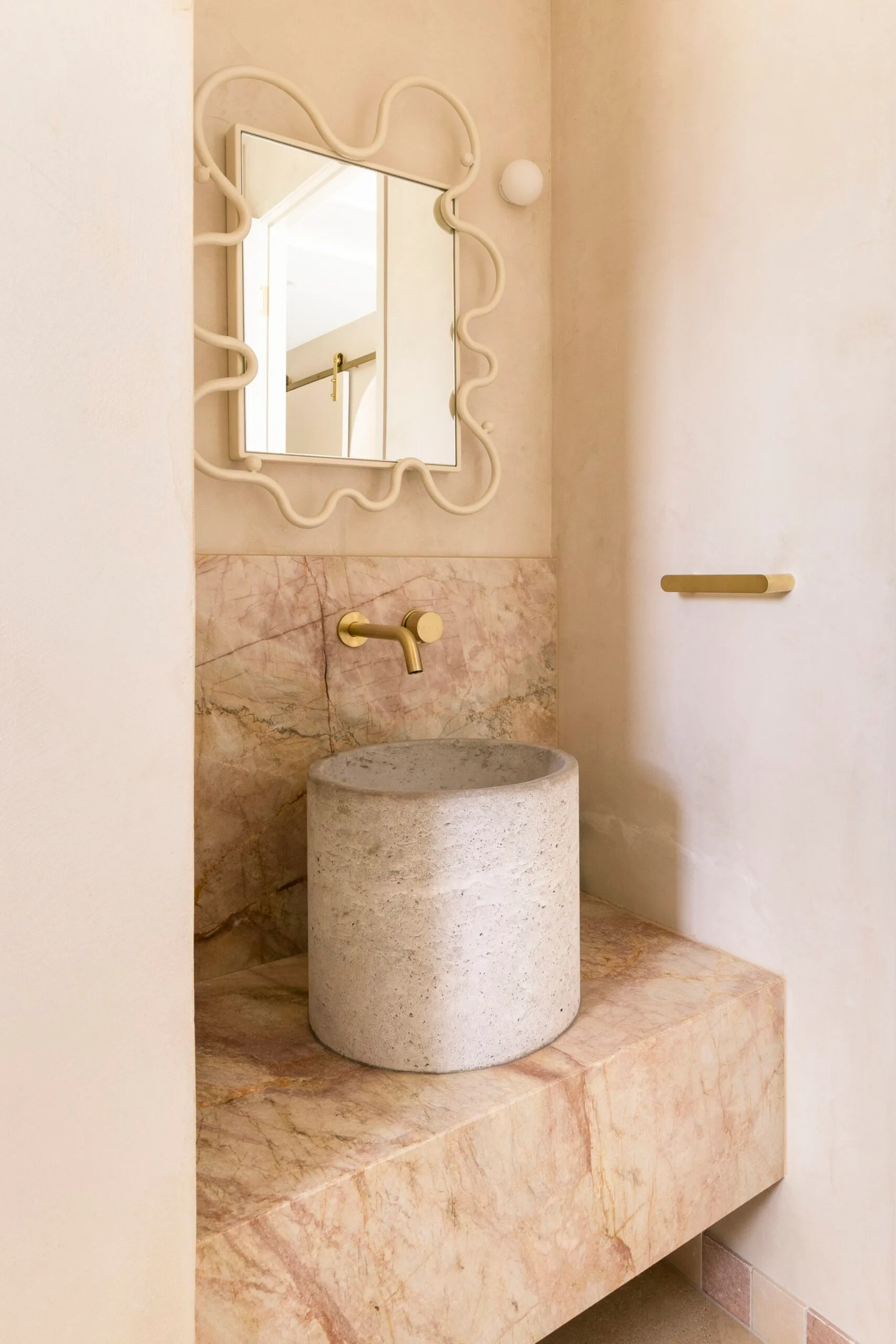 Elegant bathroom with a stone sink, artistic mirror, and brass faucet on a marble counter.