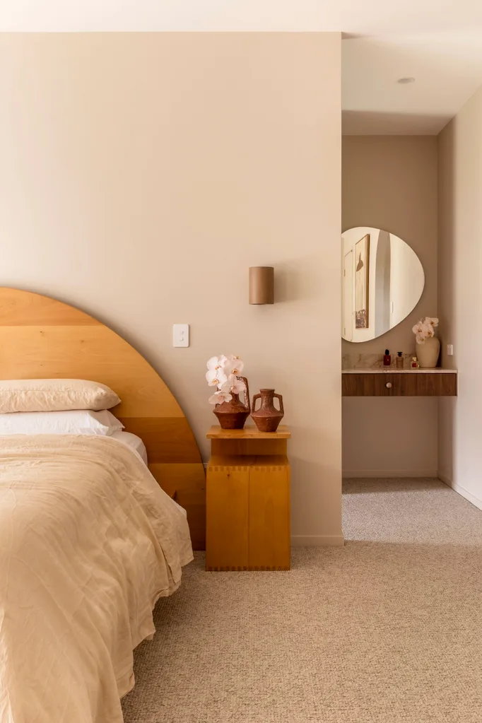 Cozy bedroom with wooden bed and bedside table, beige bedding, pottery decor, and a round mirror in the background.