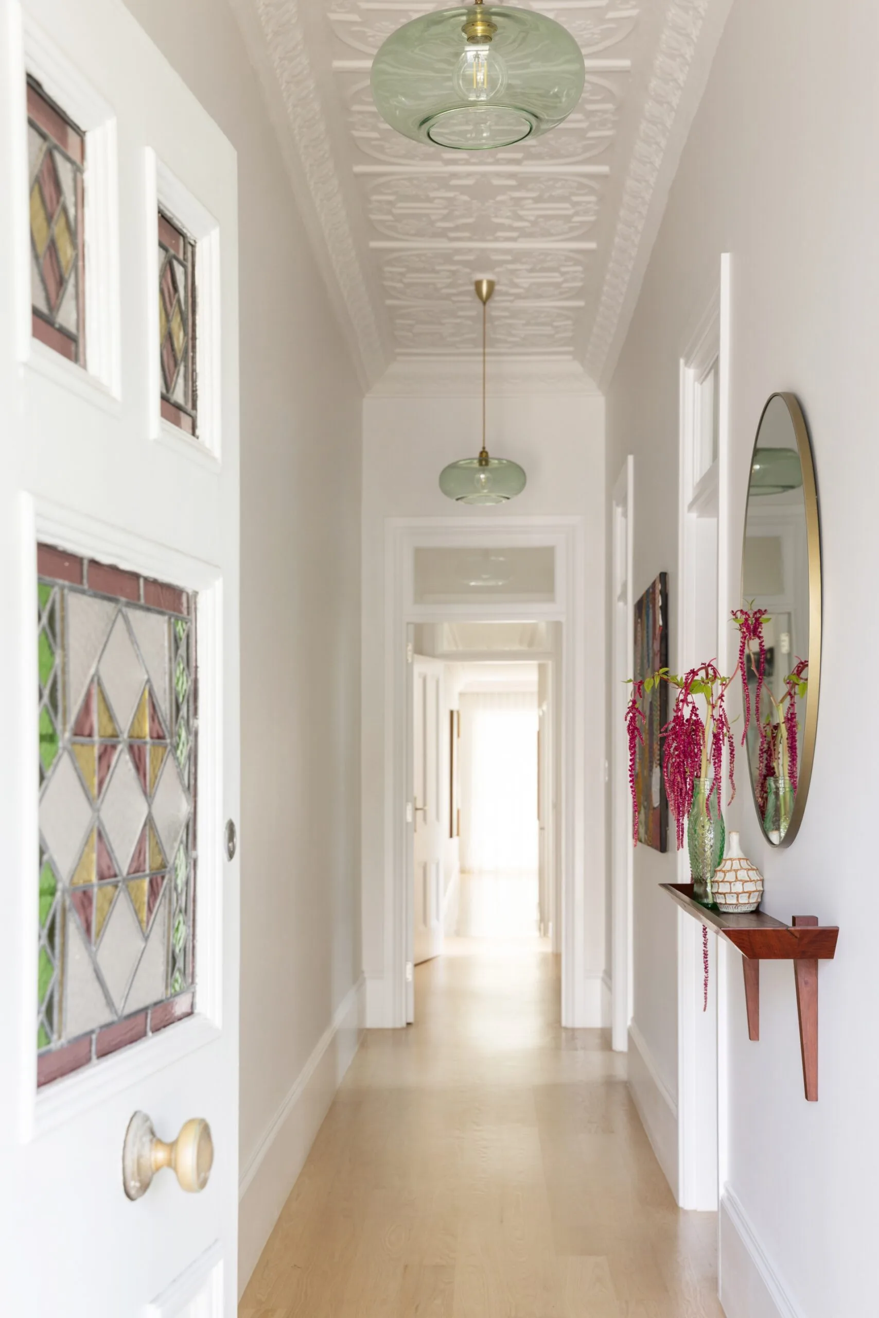 Elegant hallway with decorative ceiling, stained glass door, pendant lights, and a shelf with vases and mirror.
