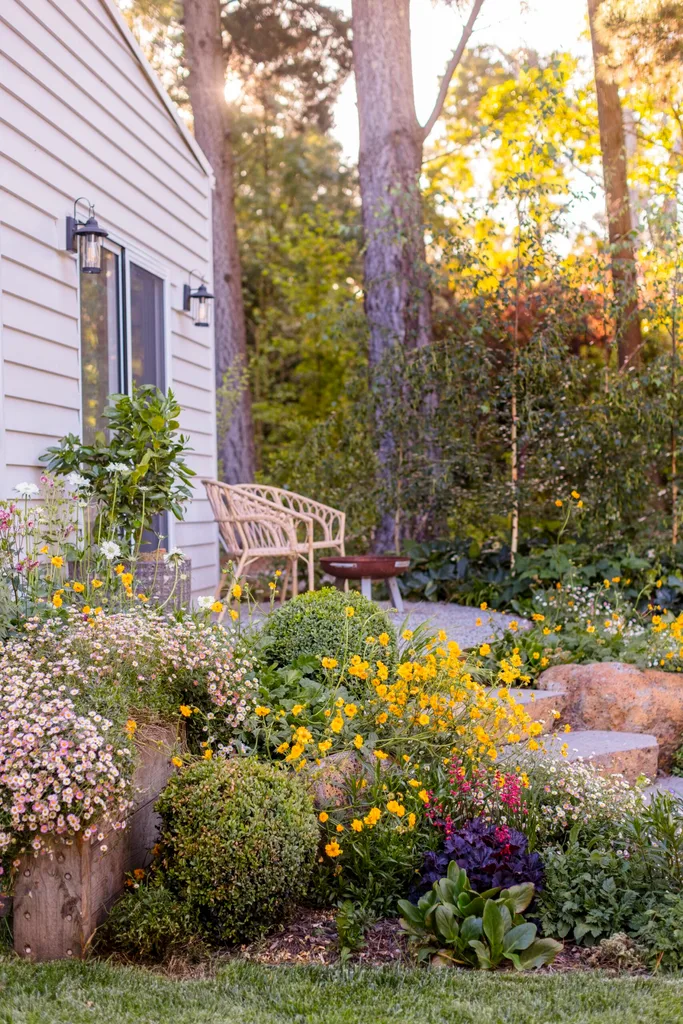 Sunny garden with colorful flowers near a house, featuring a wooden bench and lush greenery in a peaceful setting.