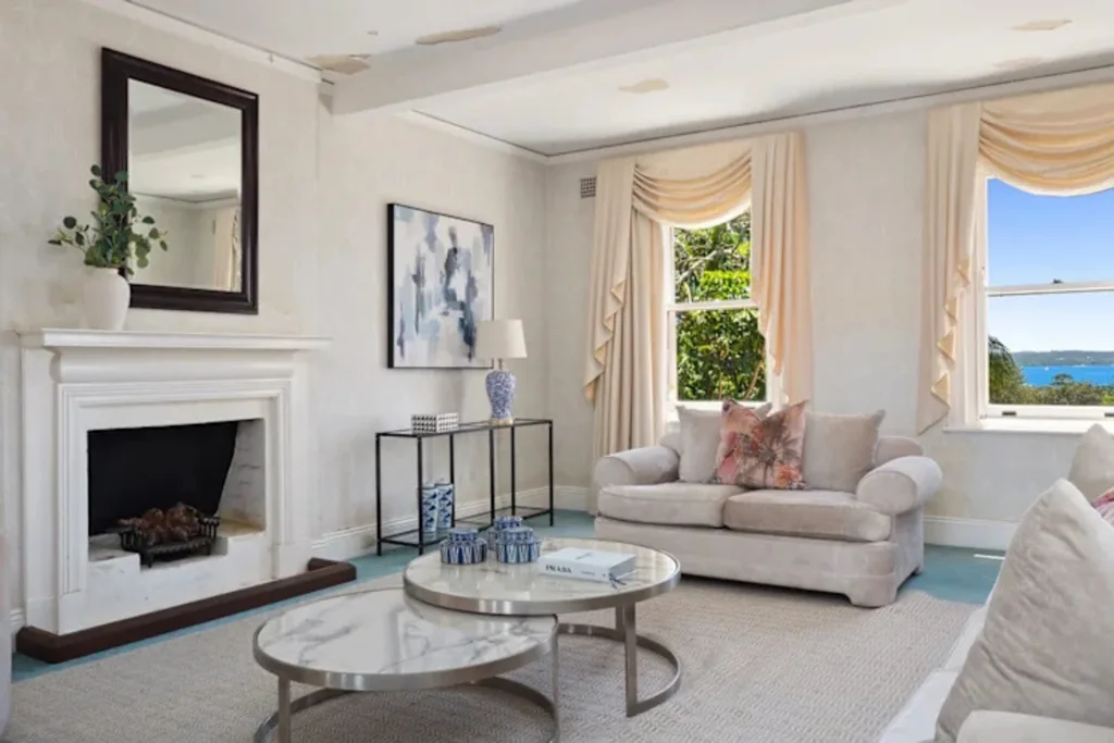 Elegant living room with beige sofa, fireplace, abstract artwork, and large windows overlooking greenery and water.